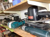 Shelf with Craftsman orbital sander, Mastercraft right angle drill, Black & Decker cordless driver with attachment, showing condition and positioning.