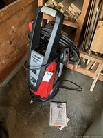 Full view of Husky electric pressure washer standing upright with hose wrapped around handle and manual on the floor