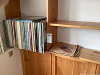 Shelf with over 80 vintage LP records standing vertically, showing album spines in various colors and styles. To the right, a small stack of old 78rpm records in paper sleeves.