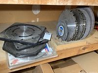 Multiple circular saw blades stacked on shelf including some in plastic holders and a stack of diamond abrasive cutting discs.