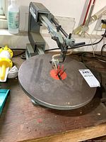 Image showing the round worktable and adjustable arm of the scroll saw on a wooden surface.