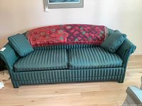 Front view of the dark green striped sofa bed with cushions and red decorative throw on backrest.