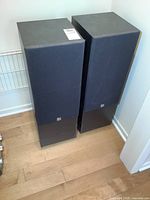 Pair of KEF C75 tower speakers standing on wood floor beside wall, with minor wear visible on sides and tops.