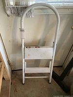 Front view of white folding metal step ladder showing two steps and curved handle for support.