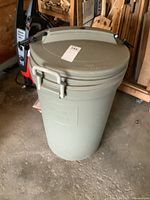 Front and side view of large beige Rubbermaid Animal Stopper trash can standing on concrete floor in garage or workshop area.
