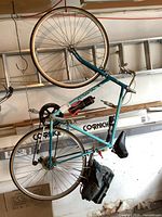 Full view of the vintage blue Norco 12-speed bicycle hanging on a hook, showing frame, wheels, saddle bag, and pump.