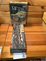 Photo showing vintage diecast MG-TC car model box next to the Bismarck battleship model box on wooden surface.