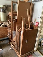 Wood rack filled with various wood pieces including large flat panels and long planks, plus visible plexiglass sheets. Rack made of wood with wheels for moving.