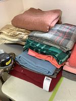 Stack of 9 wool blankets showing a variety of colors and folded neatly.