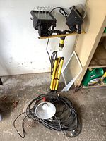 Full view of the tripod stand holding two halogen floodlights, and coiled extension cord with reflector lamp on the ground.