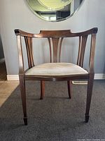 Front view of antique Edwardian mahogany tub chair showing curved inlaid backrest and beige upholstered seat.