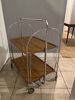 Front view of the tea cart showing the two molded plywood shelves within polished chrome frame on caster wheels.