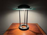 Postmodern saucer table lamp on wooden surface, lamp off showing saucer glass top and metal frame.