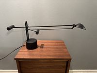 Side view of the desk lamp showing the long adjustable arm with counterweight and round base on a wooden surface against grey wall.