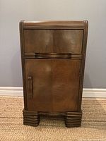 Front view of the vintage Art Deco nightstand showing the drawer and cabinet door with carved wood, waterfall top edges, and stepped base.
