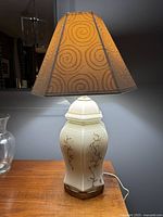 Full view of the vintage ceramic ginger jar table lamp with beige swirl-patterned fabric shade, illuminated and placed on a wooden surface.