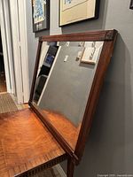 Full view of mahogany framed beveled mirror resting on a wood table against a wall.