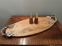 Full view of the wood serving tray with pewter grape vine handles and teak salt and pepper shakers placed on top.