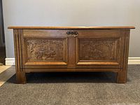 Front view of vintage solid oak chest showing hand carved wildlife panels and brass handle