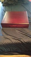 Wooden polished reddish-brown box with bordered top panel on a dark fabric background.