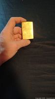 Photo of a brass Zippo lighter held in hand showing front face with scratches and wear.
