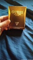 Front view of Guess Seductive Homme cologne in original brown and gold package being held by hand.