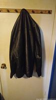 Photo of the black leather jacket hanging on wall hooks, showing front and side views.