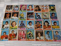 Photo showing 31 1974-75 OPC hockey cards spread out on a white surface. Players from multiple NHL teams are featured in colorful card designs.