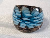 Close-up photo of the black art glass ring with blue and white petal shapes on a white fabric background.