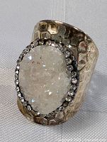 Front view of hammered silver-tone ring with raw white druzy-style stone center and clear rhinestone halo around the stone.