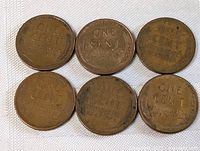Six vintage American one-cent wheat pennies arranged in two rows on a cloth surface showing natural patina and wear typical of aged copper coins.