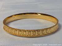 Full side view of gold plated bangle showing carved oval pattern and beaded edge decoration.