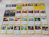 Photo showing the front side of 50 Pokémon trading cards fanned out in a grid layout, displaying various characters, trainers, and items.