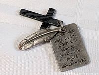 Photo showing the religious pendant charms: a black cross, a silver feather, and an engraved scripture tag with Isaiah 40:31 verse.