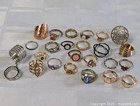 Top view of 25 mixed costume rings of various styles, materials, and sizes on a light grid background