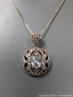 Close-up of pendant showing large central clear stone and detailed design with smaller stones and milgrain edges.