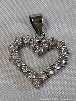 Front view of sterling silver heart pendant encrusted with clear cubic zirconia stones on textured surface background