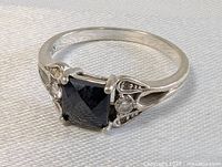 Front angled view showing the square black onyx stone in the center with two clear round stones on each side and silver detailing on the band.