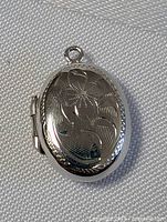 Close-up photo of the sterling silver oval pendant locket with floral engraved design on the front and a hanging loop on top.