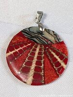Front view of the round stone pendant highlighting red and cream spine-like pattern with gray marbled top section and attached sterling silver clasp.