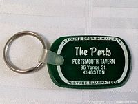 Green rectangular tavern promotional keychain with white text and clear clip attached to metal ring.