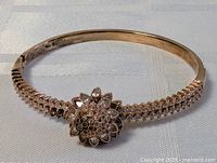 Front view of vintage gold plated bracelet showing floral cluster centerpiece encrusted with stones and detailed stone rows on band.