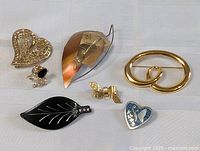 Photo showing six vintage brooch pins of various designs and materials displayed on white fabric.