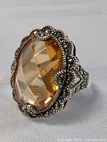 Close-up angled view of vintage silver ring with large faceted orange stone and detailed silver beadwork on setting and band.