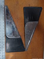 Two rubber mud flaps with attached metal plates laid flat on wooden surface with ruler for scale.