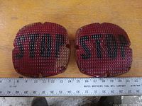 Two red square tail light lenses with textured grid and STOP printed in black text. Placed next to a ruler for size reference.