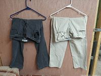 Two pairs of women's jeans on hangers, one dark gray and one cream colored, displayed against a wooden background.