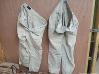 Two pairs of beige women's jeans hanging on a wooden surface, front and side views visible.