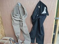 Both pairs of jeans, beige and black, folded and leaning against a wooden background to show their color, style, and condition.
