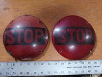Pair of red round stop tail light lenses side by side showing 'STOP' text and approximate size with ruler.